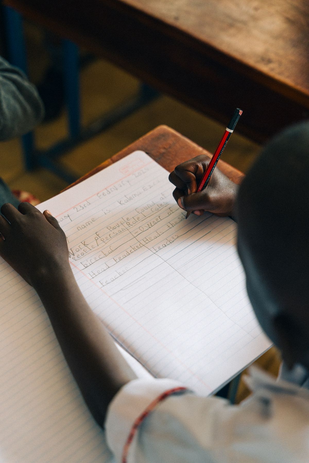 A pupil's hand writing in an exercise book with a pencil