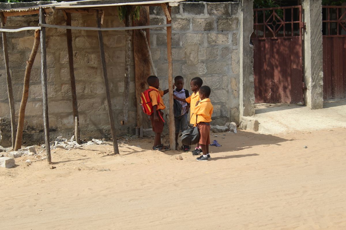 Boys in orange school uniforms with backpacks outside a school compound